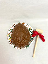 Load image into Gallery viewer, A chocolate egg with a heart-shaped pattern on top, presented on a plate with a wooden hammer beside it, likely indicating a砸 egg game or activity.
